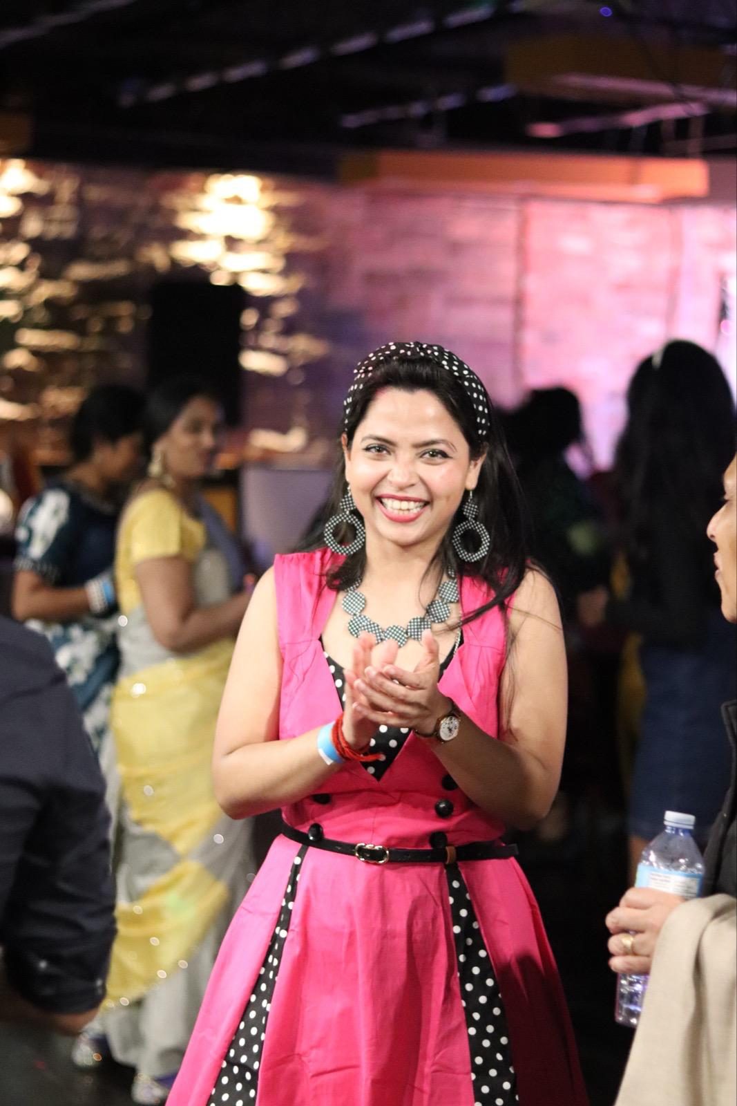 A smiling guest in a pink polka-dot 50s-style dress, headband and statement earrings, clapping