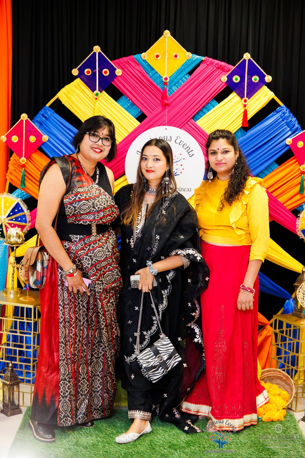 Three friends posing in front of the Luminous Events kite backdrop
