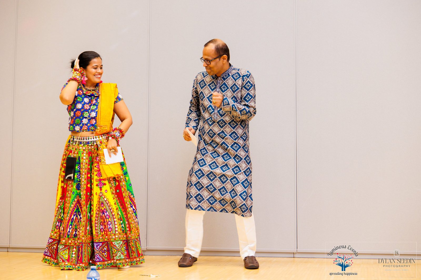 Two guests in festive outfits on stage holding envelopes during the event program