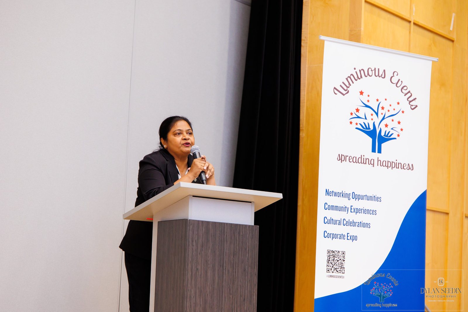 A speaker addressing guests at the podium beside the Luminous Events banner