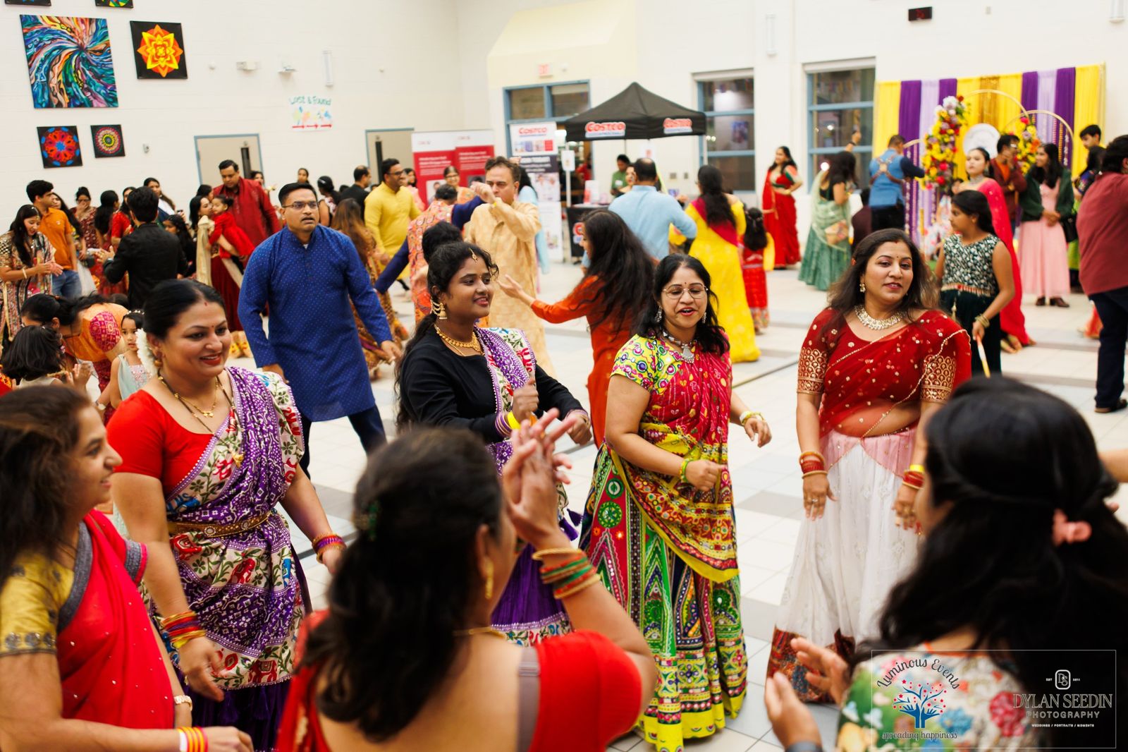 Men, women and children dancing together in a crowded hall in festive outfits