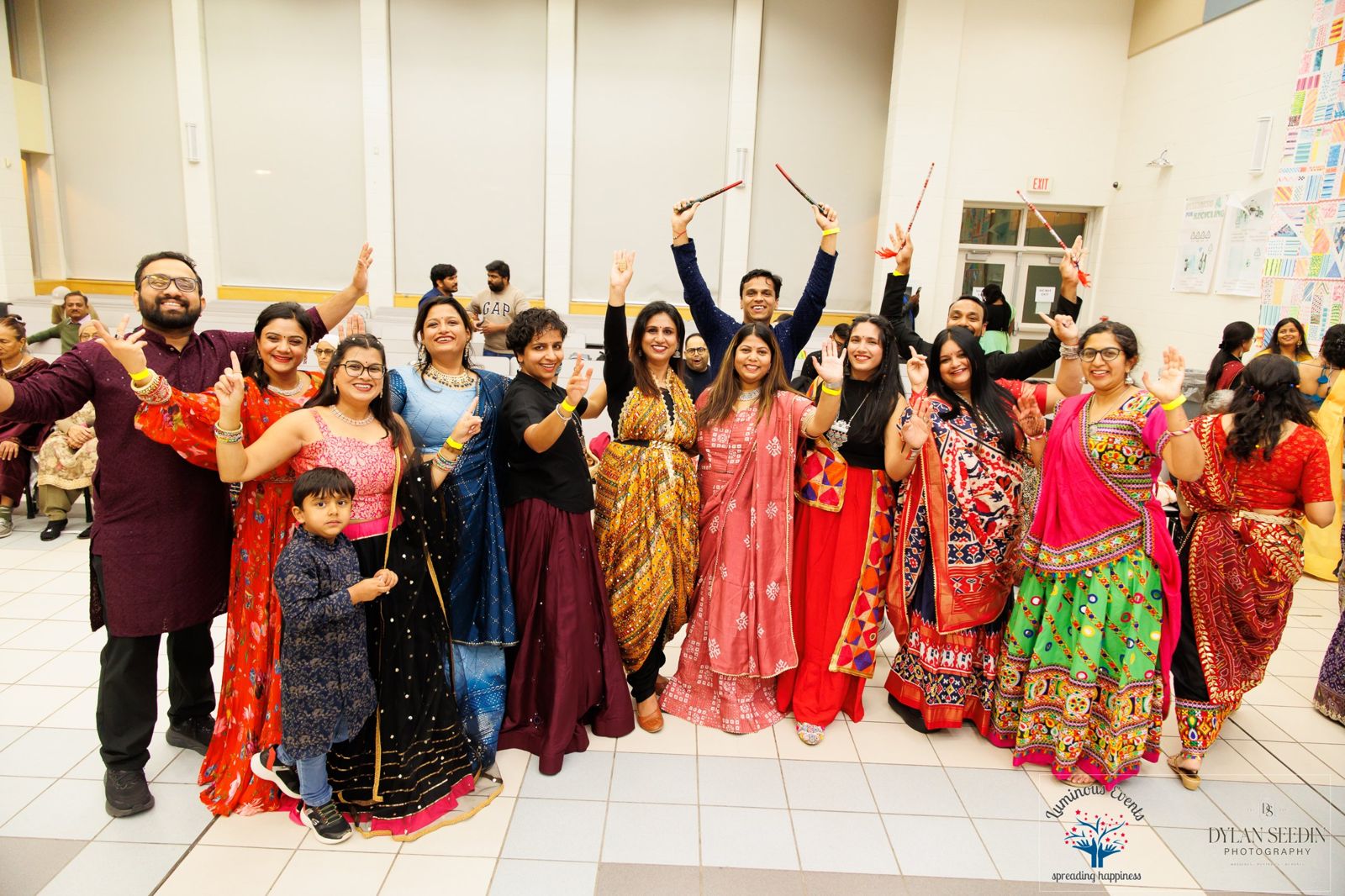 A cheerful mixed group of adults and a small child posing with dandiya sticks raised
