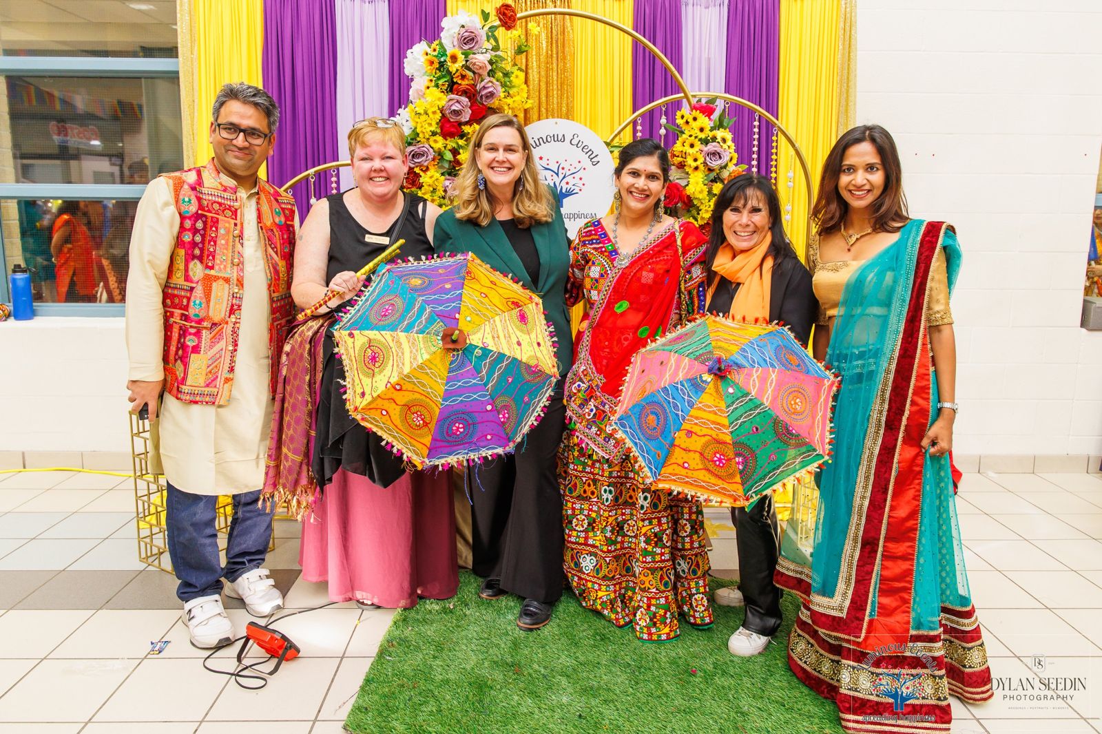 Honoured guests and organizers smiling with colourful embroidered umbrellas at the floral Luminous Events backdrop