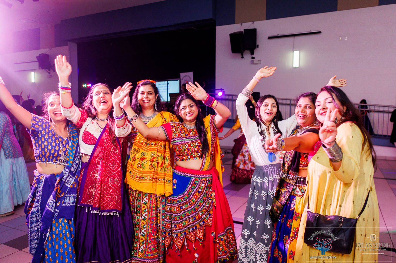 Women in bright traditional outfits waving and smiling on the dance floor during the Neon Hour