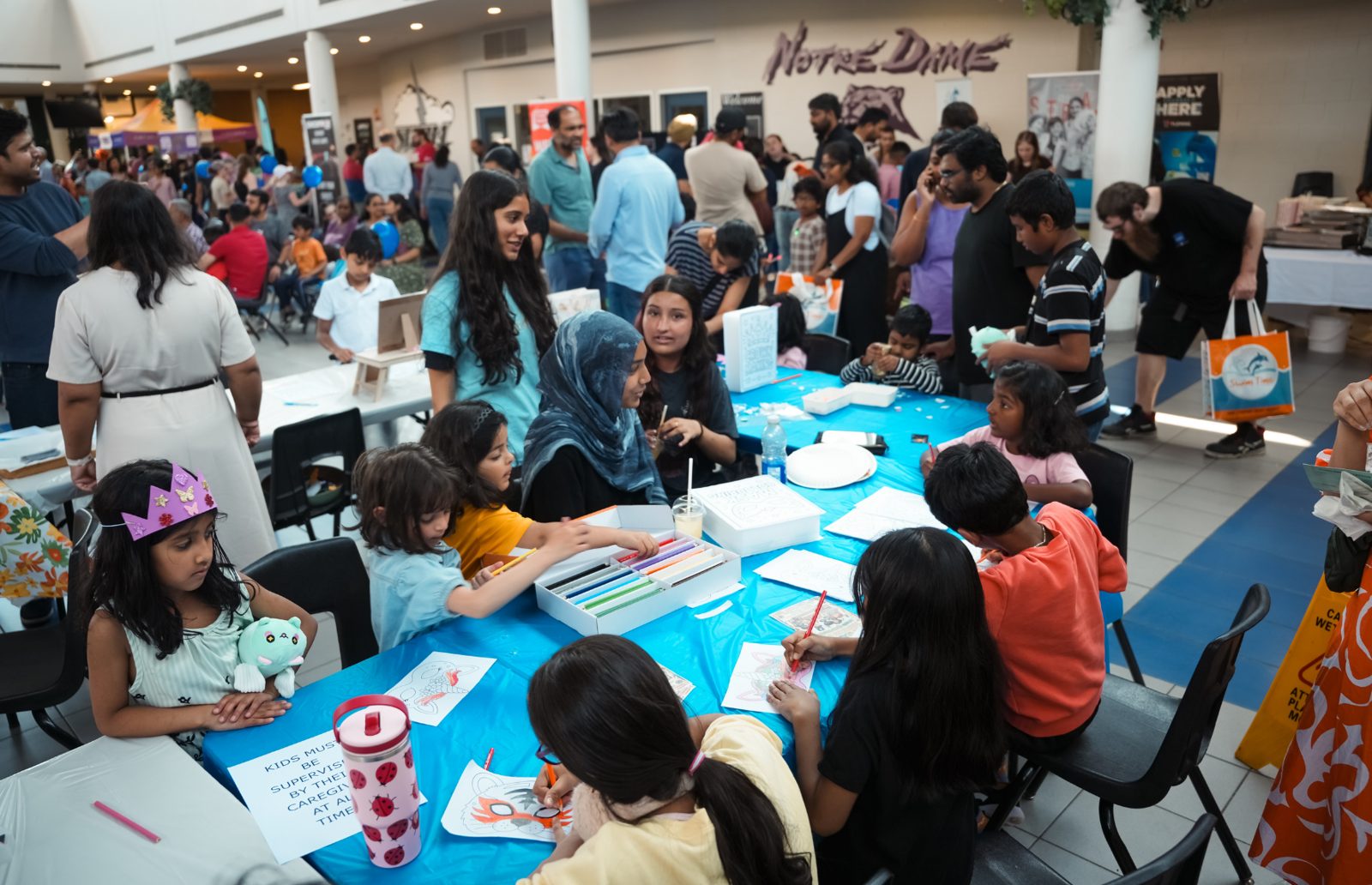Children colouring and making masks at a long blue table in the free art workshop