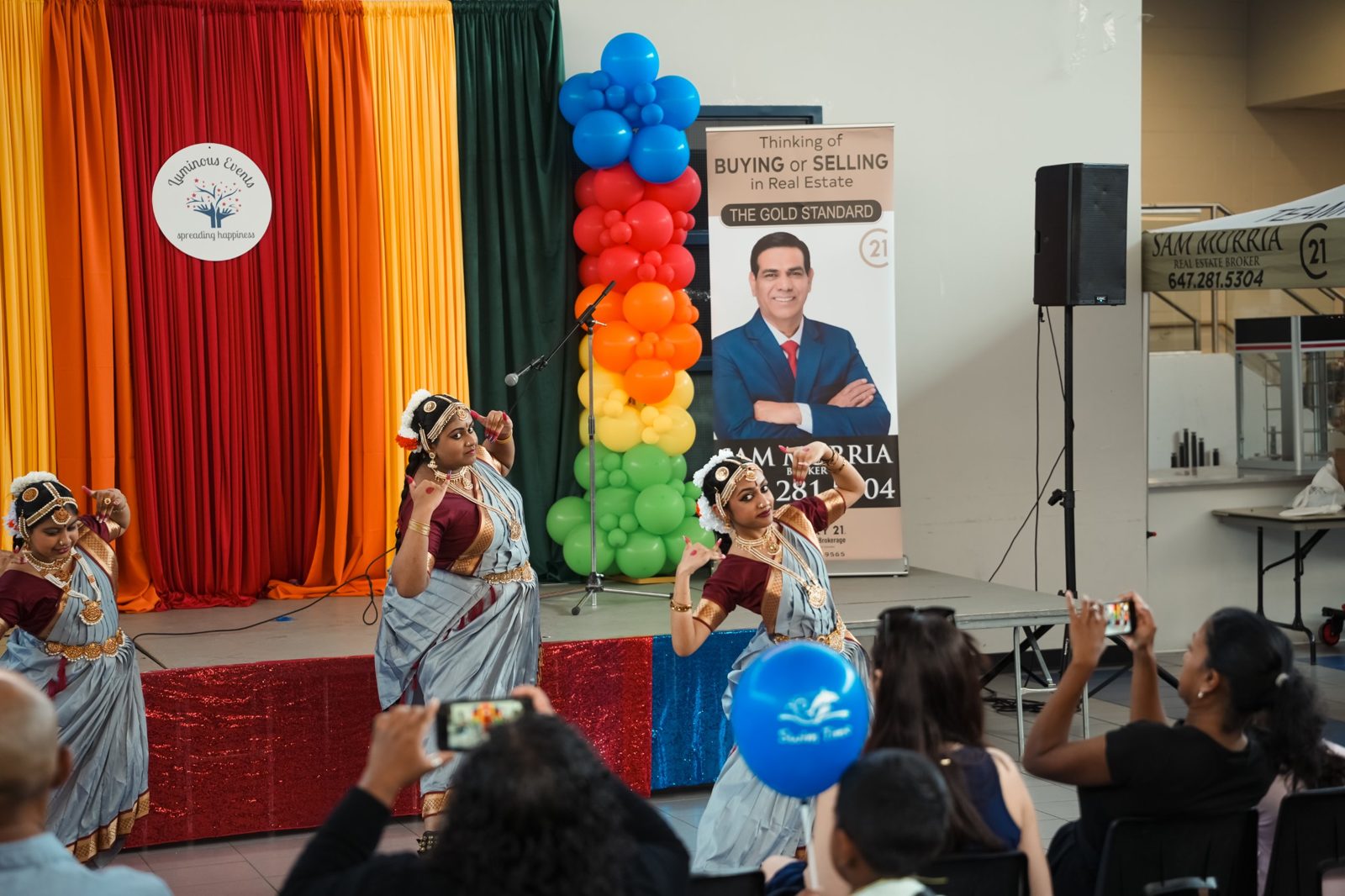Classical dancers in grey and maroon costumes performing on stage while guests film on their phones