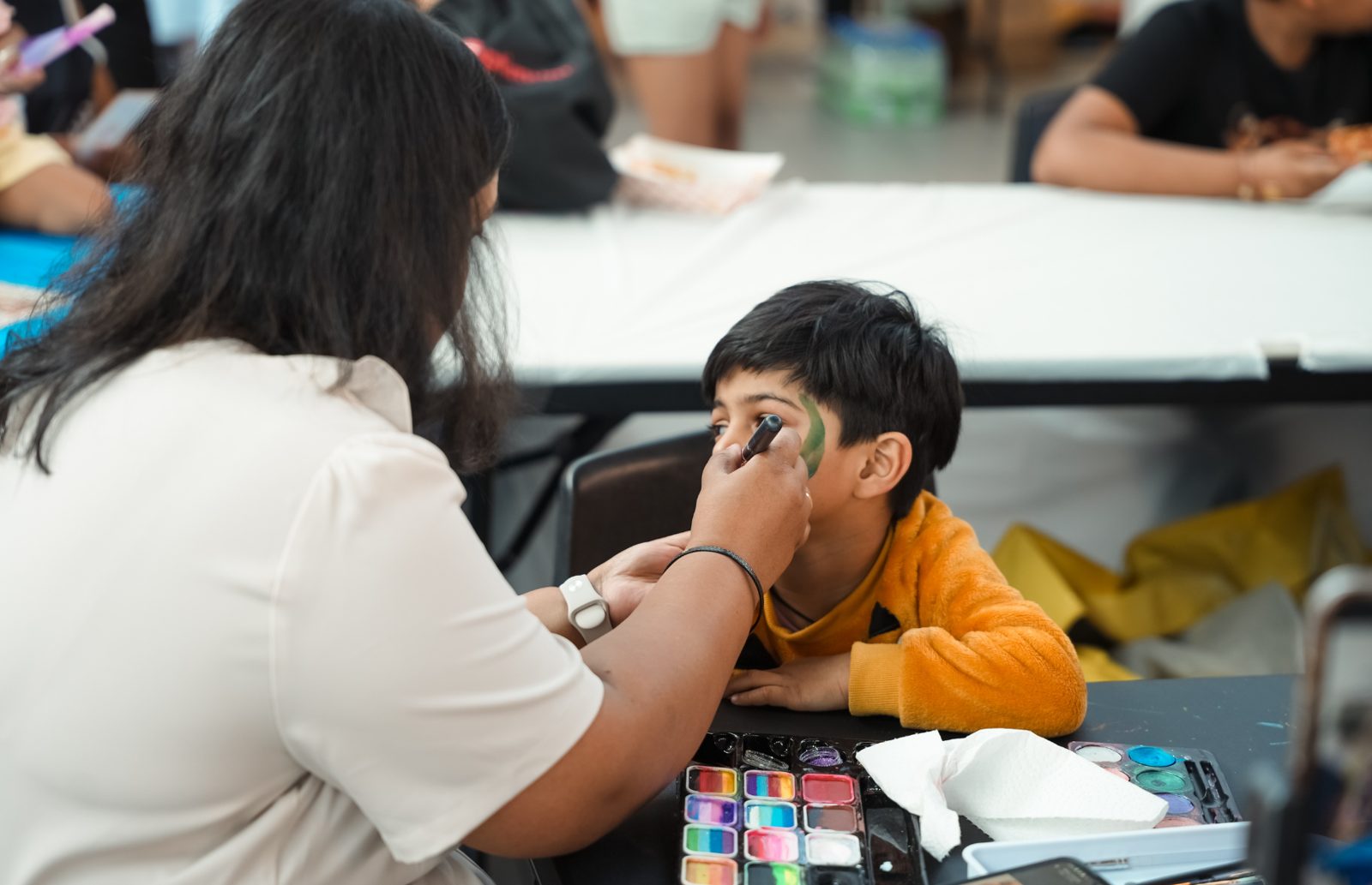 A young boy having his face painted at the face painting table