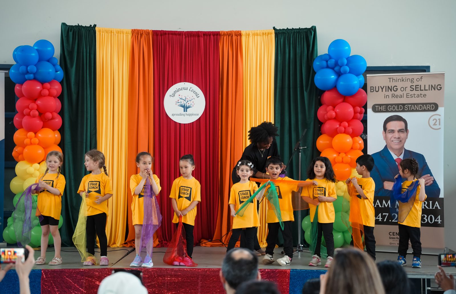 Children in yellow T-shirts dancing with colourful scarves in front of the rainbow balloon column