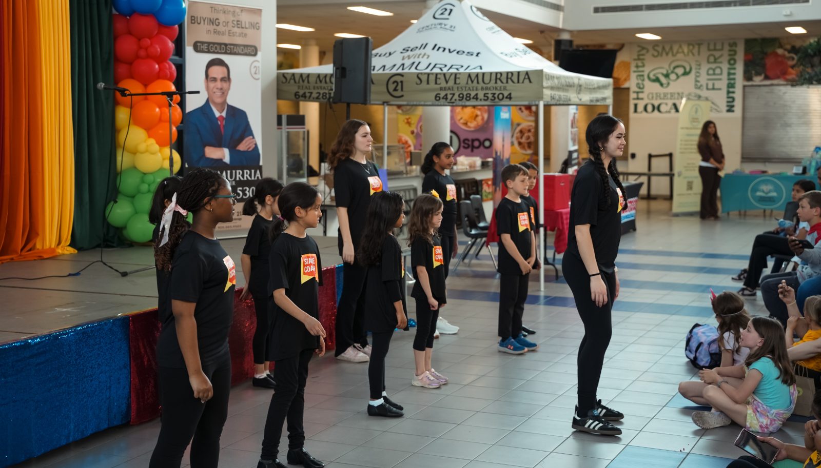 Young performers in black Stage Coach T-shirts lined up on the floor in front of the stage