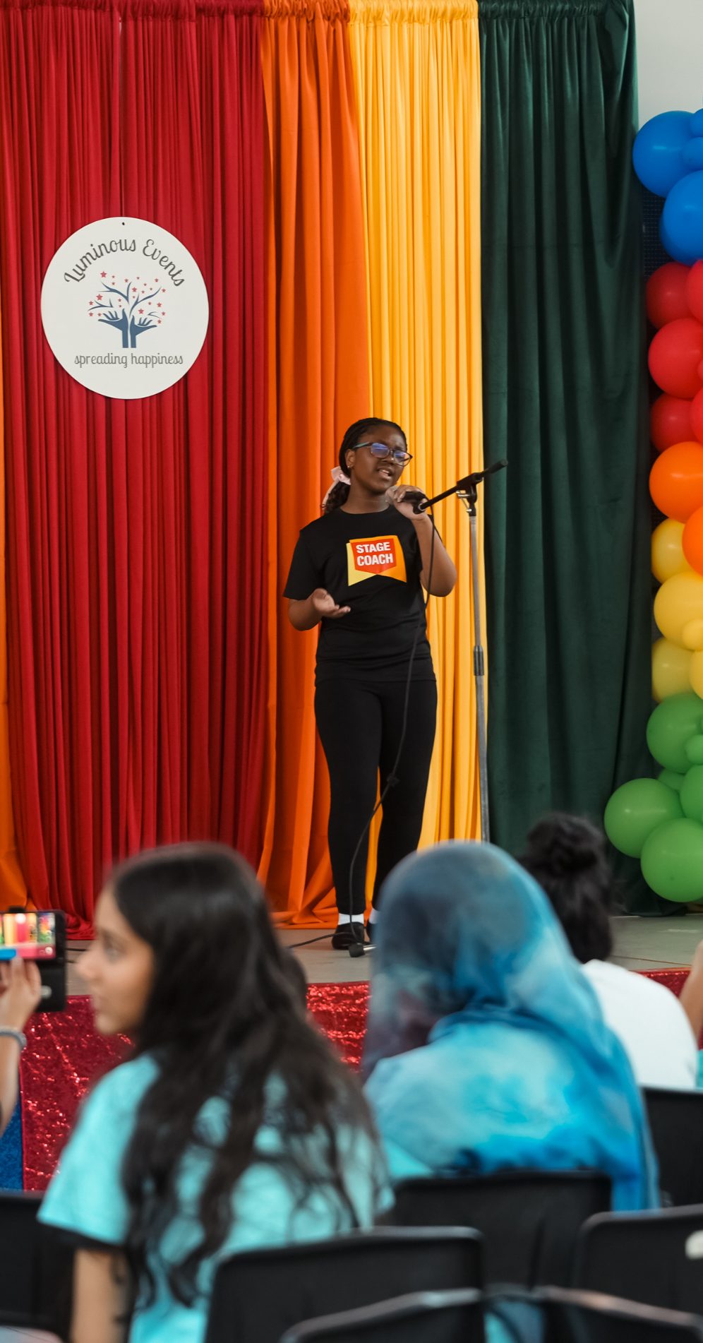 A young singer in a Stage Coach T-shirt performing at the microphone in front of the Luminous Events backdrop